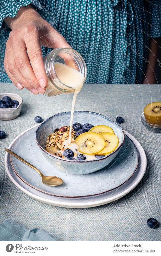 Frau gießt Milch in eine Schüssel mit Müsli eingießen melken Kiwi Frühstück Blaubeeren Vitamin selbstgemacht Mahlzeit Morgen Schalen & Schüsseln Molkerei