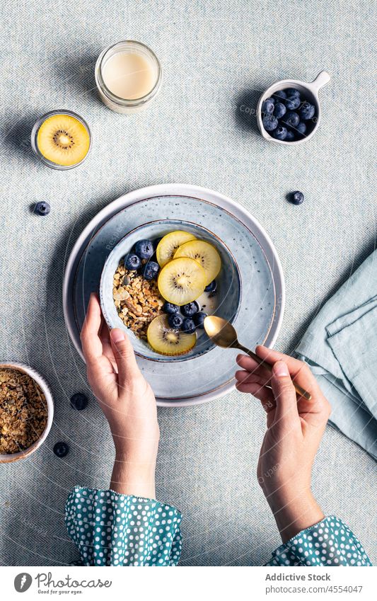 Frau mit einer Schüssel Müsli zum Frühstück Kiwi Schalen & Schüsseln Morgen Blaubeeren gesunde Ernährung Mahlzeit selbstgemacht lecker Frucht Tisch Beeren