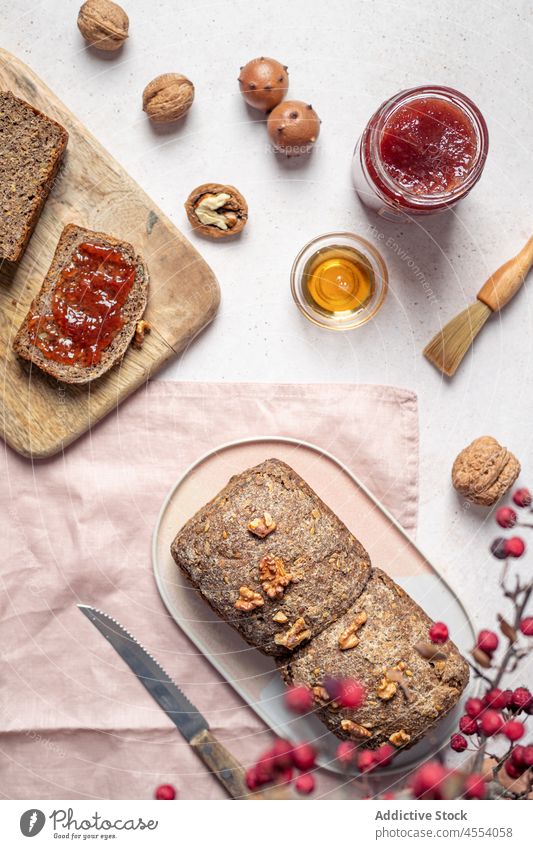 Laib Brot mit Marmelade und Honig Korn Brotlaib geschnitten gebacken selbstgemacht Walnussholz Zusammensetzung Messer Samen Spielfigur Glas süß Lebensmittel