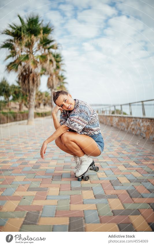 Positive Frau in Rollschuhen hockt auf dem Gehweg Rollerskate Straße sportlich Hobby Bürgersteig Aktivität hockend Training Wohlbefinden Gesunder Lebensstil