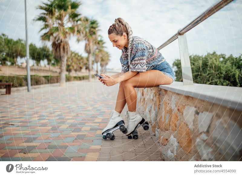 Fröhliche Rollschuhläuferin beim Surfen auf dem Smartphone Frau Rollerskate Straße sportlich Hobby Bürgersteig Gesunder Lebensstil Browsen online Funktelefon