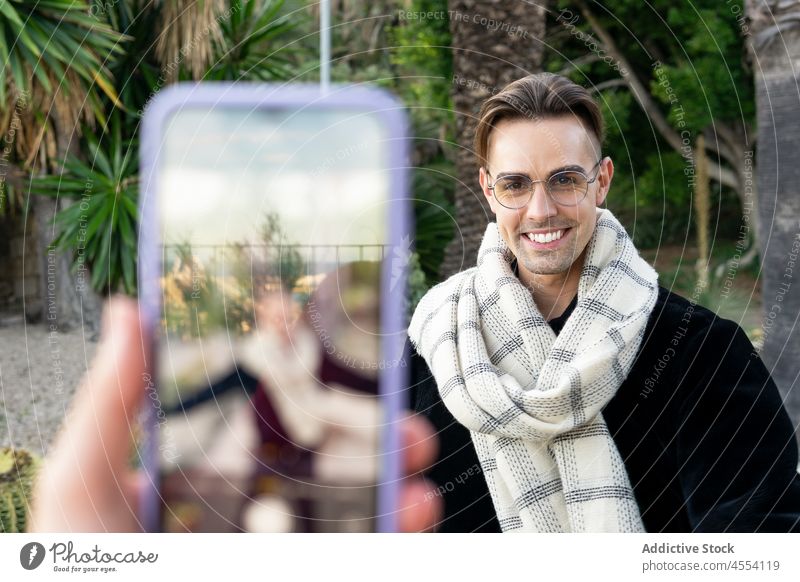 Beschnittene Person, die einen lächelnden Freund mit dem Smartphone fotografiert Mann fotografieren Lächeln Garten tropisch positiv selbstsicher Zusammensein