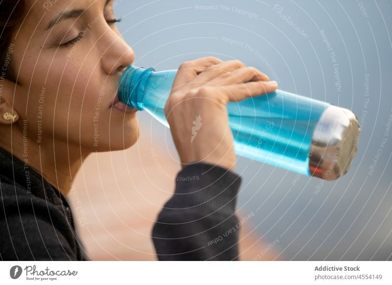 Ruhige hispanische Frau trinkt Wasser, während sie in der Nähe eines Teiches in der Natur sitzt besinnlich trinken Windstille Fluss nachdenklich Flasche See