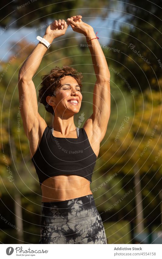 Lächelnde fitte hispanische Dame beim Aufwärmen vor dem Training im Park Sportlerin Dehnung Übung Augen geschlossen Gesundheit Frau positiv Wellness Erwachsener