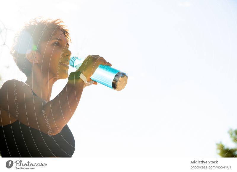 Positive hispanische Sportlerin, die beim morgendlichen Workout im Park Wasser trinkt Frau trinken Training Lächeln Athlet Gesundheit Hydrat muskulös Fitness