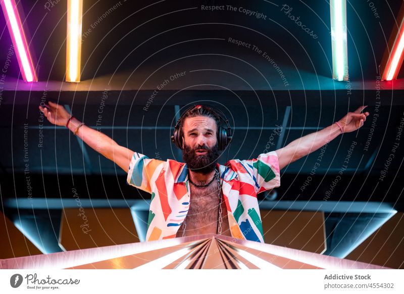 Zufriedener bärtiger DJ in einem Club mit ausgestreckten Armen während einer Party Mann dj Nachtclub selbstsicher Inhalt ausführen Musik ausdehnen Klang