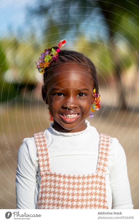 Glückliches schwarzes Kind, das in die Kamera lächelt, während es im Park im Sonnenlicht steht Lächeln Natur Stil Porträt Kindheit heiter Freude Mädchen positiv