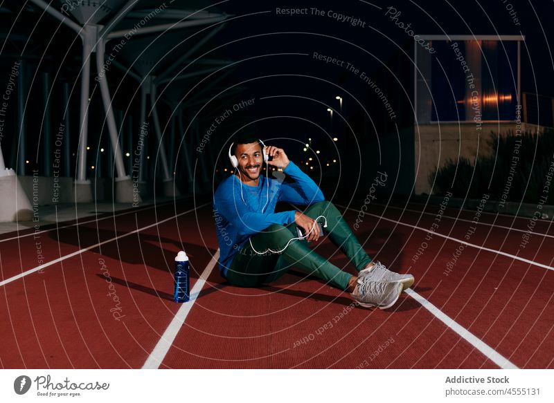Ein Sportler benutzt sein Handy und hört Musik auf dem Boden der Laufbahn jung Mann männlich Afrikanisch selbstbewusst gutaussehend Athlet benutzend Telefon