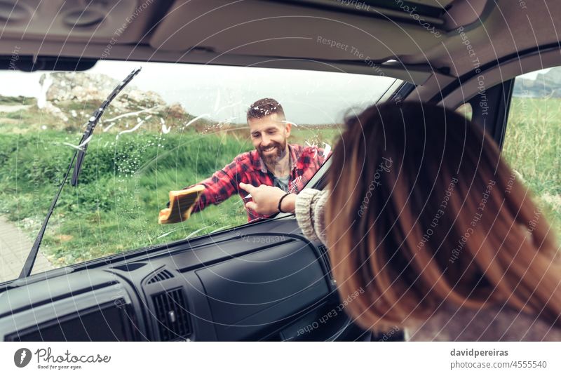 Mann reinigt die Windschutzscheibe eines Lieferwagens, während die Frau auf einen Fleck zeigt Lächeln Reinigen Spülung Glas Kleintransporter Stoff Zeigen
