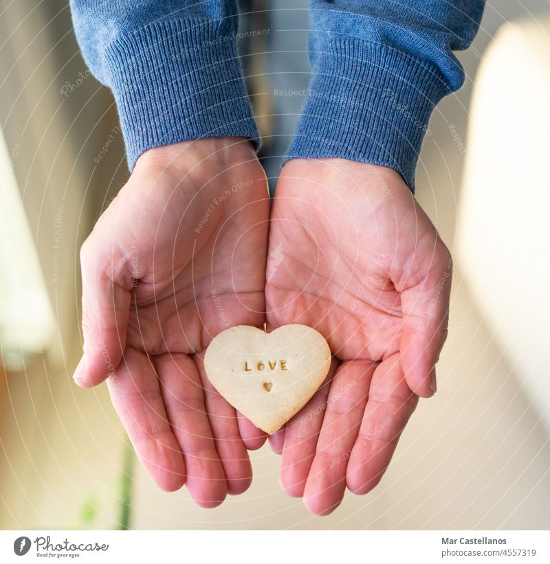 Hände mit herzförmigem Keks. Die Buchstaben LIEBE. Valentinsgruß Herz geben Geschenk Mann Liebe Briefe Lebensmittel Herzform in Händen Draufsicht Textfreiraum