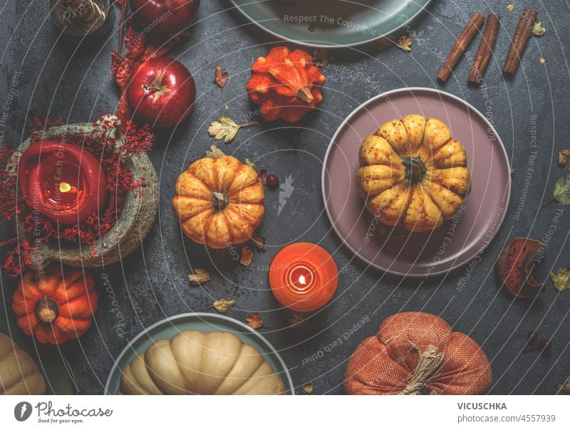Verschiedene bunte Kürbisse, Kerzen, Teller, Besteck und Dekoration auf dunklem Beton Küchentisch. Rustikales Herbststillleben mit Gemüse der Saison. Ansicht von oben.