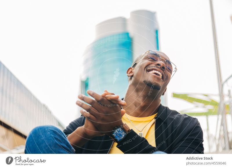Glücklicher ethnischer Mann sitzt auf einer Straßentreppe Porträt Treppenhaus ruhen heiter positiv Lächeln Schritt Lachen Laufmasche Optimist Brille Inhalt
