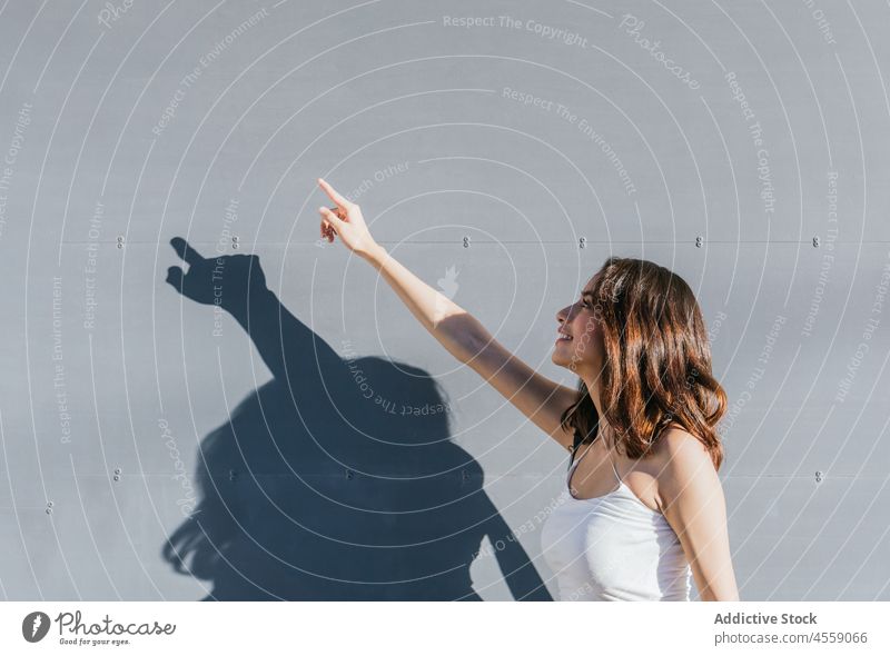 Brünette zeigt nach oben auf grauem Hintergrund Frau nach oben zeigen Aufmerksamkeit Zeigefinger gestikulieren Zeichen Wand Inhalt Lächeln heiter expressiv
