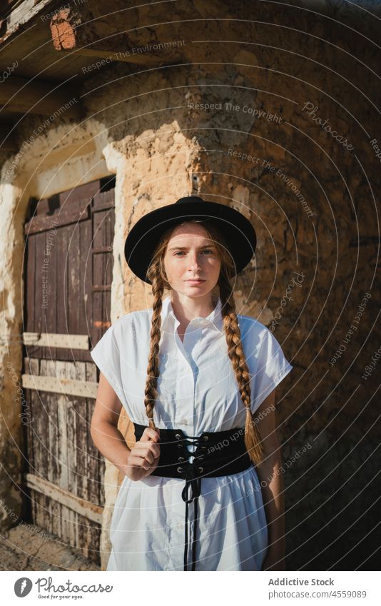 Junge Frau mit Zöpfen steht in der Nähe eines alten Steingebäudes selbstbewusst Geflecht Gurt Straße Wand Porträt Accessoire Leder ernst Kleid Tür Gebäude
