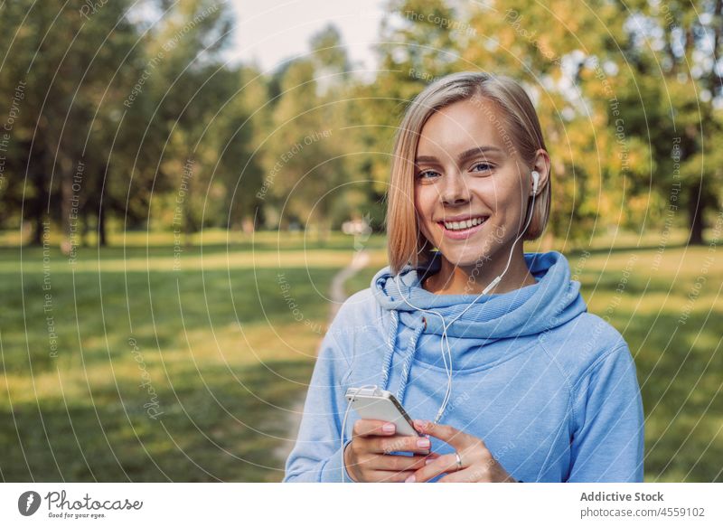 Junge Frau hört Musik über Kopfhörer auf einem Smartphone zuhören Apparatur Porträt Park Gerät Kapuzenpulli Melodie Mobile Klang Audio Gesang Telefon benutzend