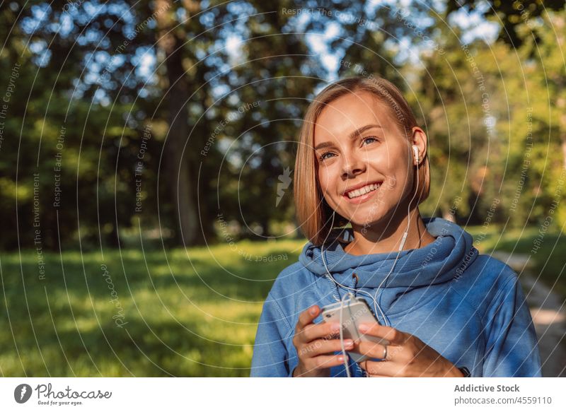 Junge Frau hört Musik über Kopfhörer auf einem Smartphone zuhören Apparatur Porträt Park Gerät Kapuzenpulli Melodie Mobile Klang Audio Gesang Telefon benutzend