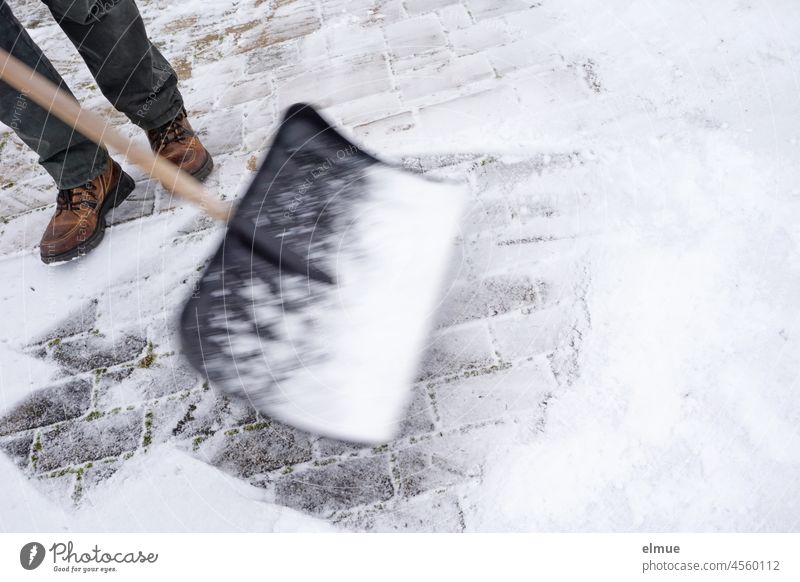 Schneeschippen - ein Mann befreit eine gepflasterte Einfahrt mit einem Schneeschieber vom Neuschnee / Winter / Bewegungsunschärfe Energieverbrauch sportlich