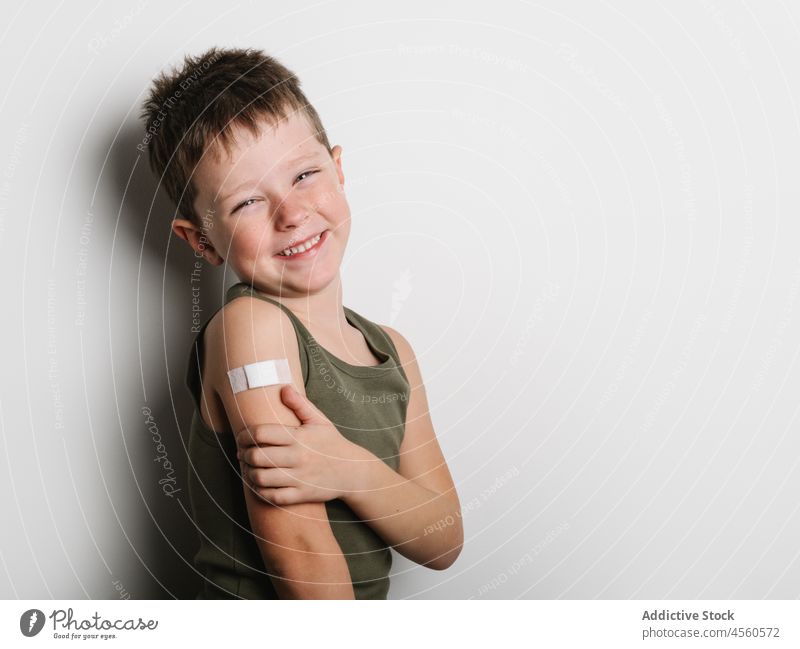 Fröhlicher Schuljunge nach der Impfung mit Pflaster am Arm Junge Kind Impfstoff heiter Stoß Schuss Einspritzung Gesundheit Arme Motivation Kindheit abstützen