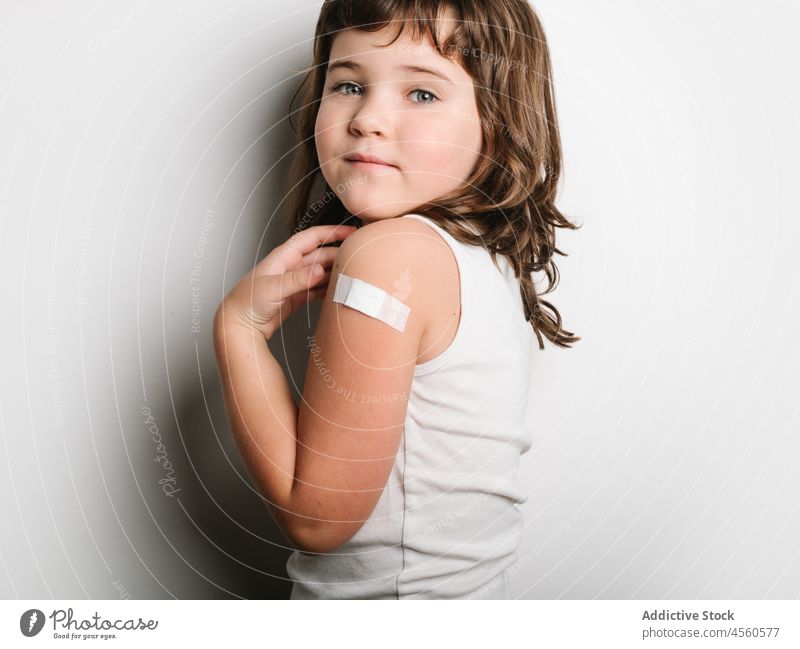 Ernsthaft geimpftes Mädchen mit Pflaster am Arm Schulmädchen bandagieren Band Impfstoff behüten Virus Impfung Stoß Glück Lächeln Schuss Sicherheit