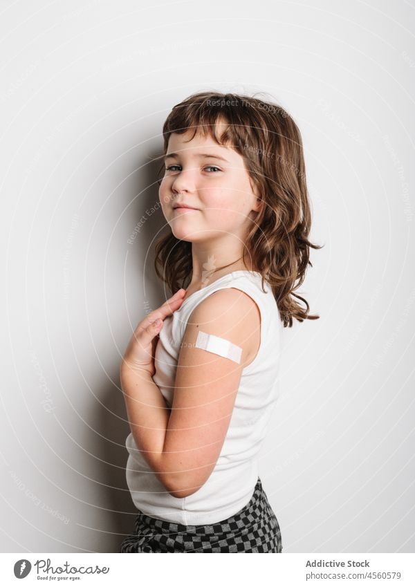 Ernsthaft geimpftes Mädchen mit Pflaster am Arm Schulmädchen bandagieren Band Impfstoff behüten Virus Impfung Stoß Glück Lächeln Schuss Sicherheit