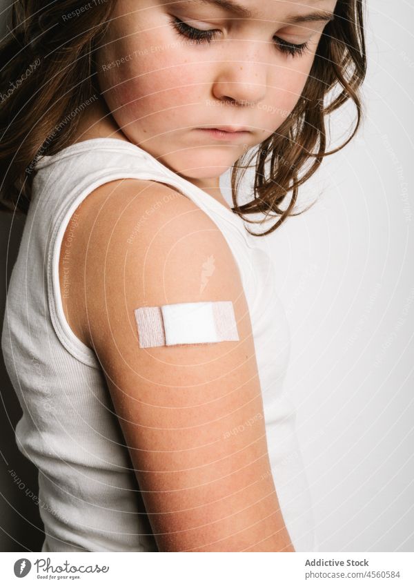 Ernsthaft geimpftes Mädchen mit Pflaster am Arm Schulmädchen bandagieren Band Impfstoff behüten Virus Impfung Stoß Schuss Sicherheit Gesundheitswesen