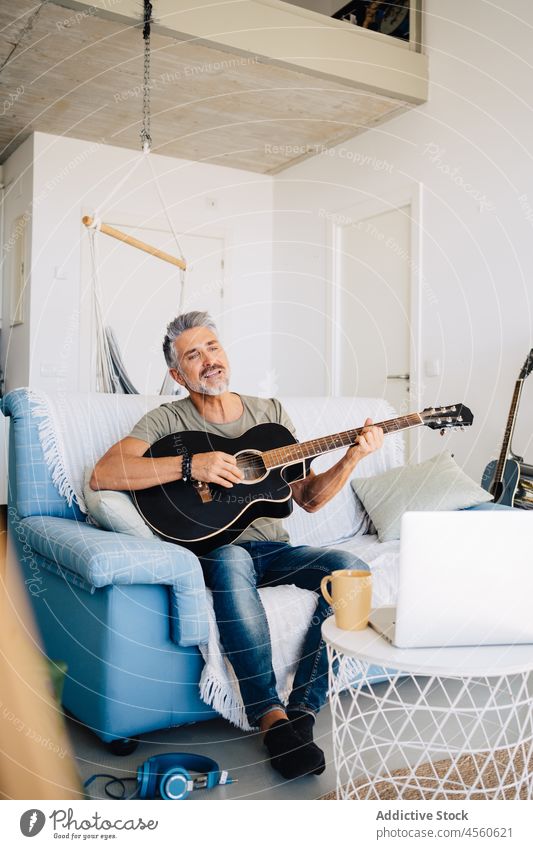 Älterer Gitarrist, der auf dem Sofa neben einem Laptop Musik macht Mann Gitarrenspieler Musiker Loft Instrument Zeichen Innenbereich akustisch spielen online