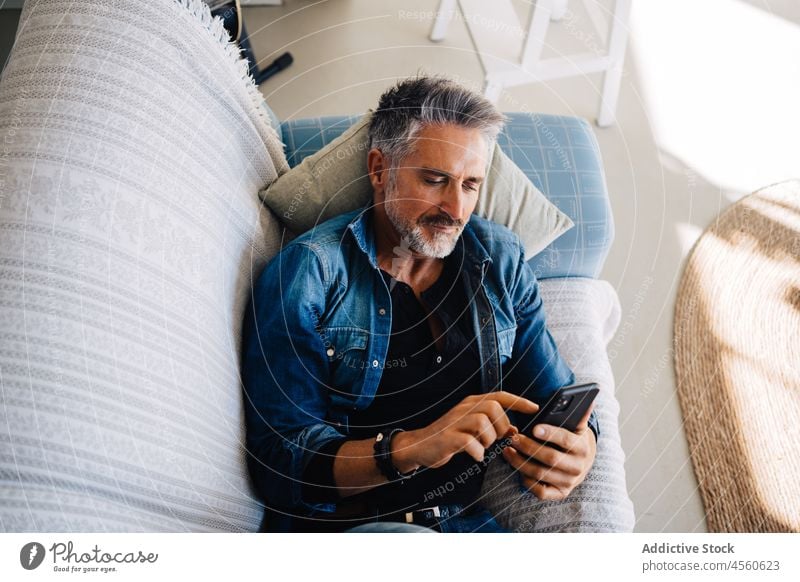 Älterer Mann, der auf der Couch liegend sein Handy durchsucht Smartphone Mobile Sofa Browsen benutzend Stil Loft Kälte ruhen Liege Zeitvertreib Funktelefon