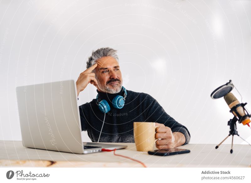 Älterer Blogger ruht sich mit einer Tasse Tee im Studio aus Mann trinken Podcast Ausstrahlung Mikrofon Laptop ruhen Aufzeichnen Arbeitsbereich Becher Pause
