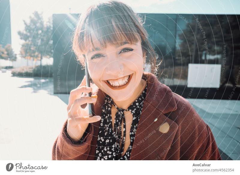 Junge schöne Geschäftsfrau in rotem Mantel, die ein Mobiltelefon benutzt und wegschaut, stehend auf der Finanzstraße. Finanzen Konzept, junges Geschäft. Lächeln in die Kamera an einem sonnigen Tag