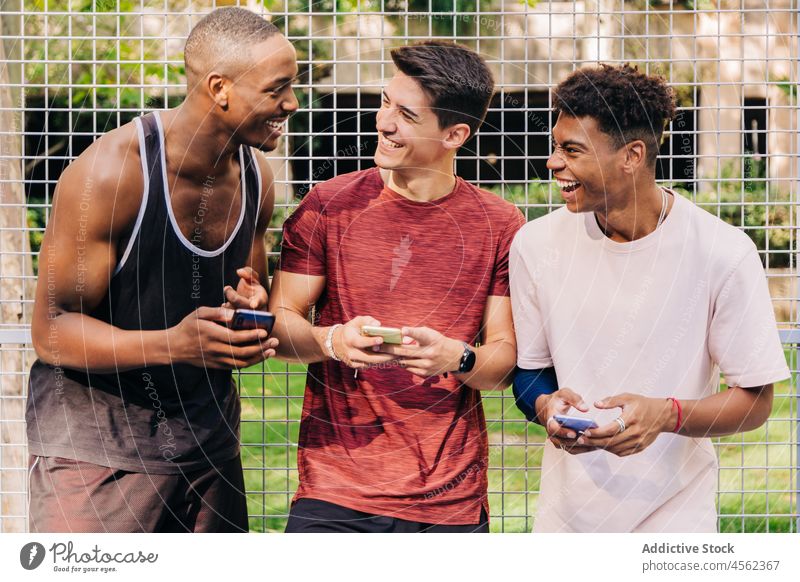 Verschiedene befreundete Sportler, die gemeinsam auf Smartphones surfen und auf dem Sportplatz lachen Menschengruppe Browsen Freund Athlet heiter passen