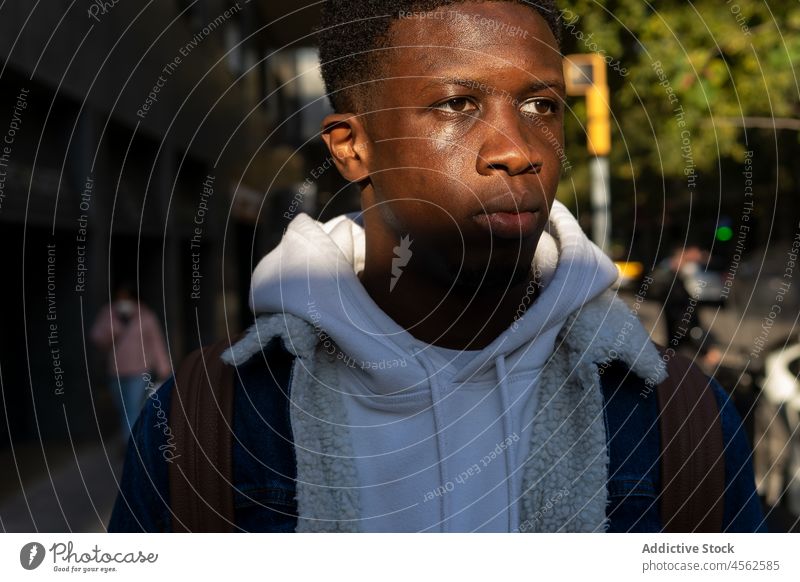 Ernster schwarzer Mann steht auf der Straße im Sonnenlicht trendy ethnisch Vorschein Individualität selbstbewusst ernst besinnlich männlich Afroamerikaner