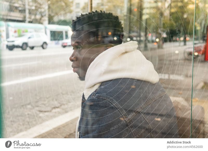 Nachdenklicher schwarzer Mann sitzt an der Bushaltestelle auf der Straße besinnlich nachdenklich warten Großstadt urban Stil männlich Afroamerikaner ernst