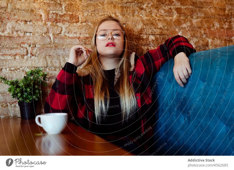 Junge Frau sitzt auf einer Couch in einem Cafe Porträt jung in die Kamera schauen Restaurant blond Windstille lässig Kaukasier Kleidung Kaffee Kaffeehaus