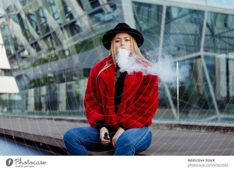 Blonde junge Frau raucht mit Vaper-Maschine auf der Straße vaping Rauchen Verdampfer Erwachsener alternativ attraktiv schön Hut blond Schlag Kaukasier Zigarette