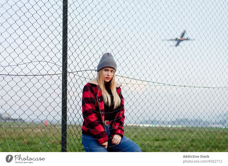Junge Frau lehnt an einem Zaun in der Nähe des Flughafens jung Porträt in die Kamera schauen posierend Herbst niedlich horizontal Lehnen Freizeit Lifestyle