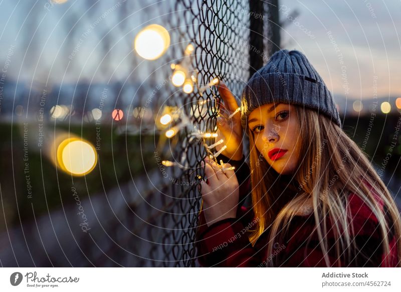 Junge Frau lehnt sich an den Zaun und hält eine leichte Girlande jung Porträt attraktiv Herbst blond Bokeh Glühbirnen Kaukasier Großstadt niedlich Abend