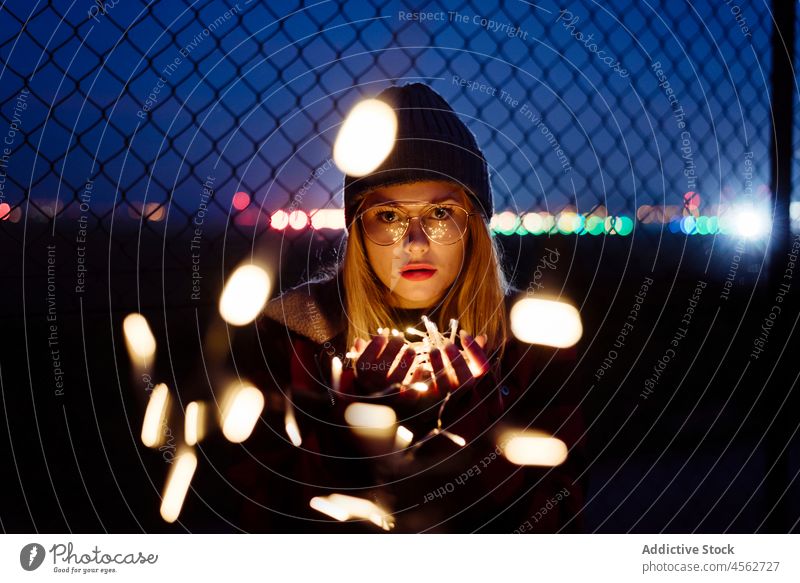Junge Frau mit Wollmütze und Brille hält eine leichte Girlande jung Nacht Porträt attraktiv Herbst blond Bokeh Glühbirnen offen Kaukasier Großstadt Kreativität