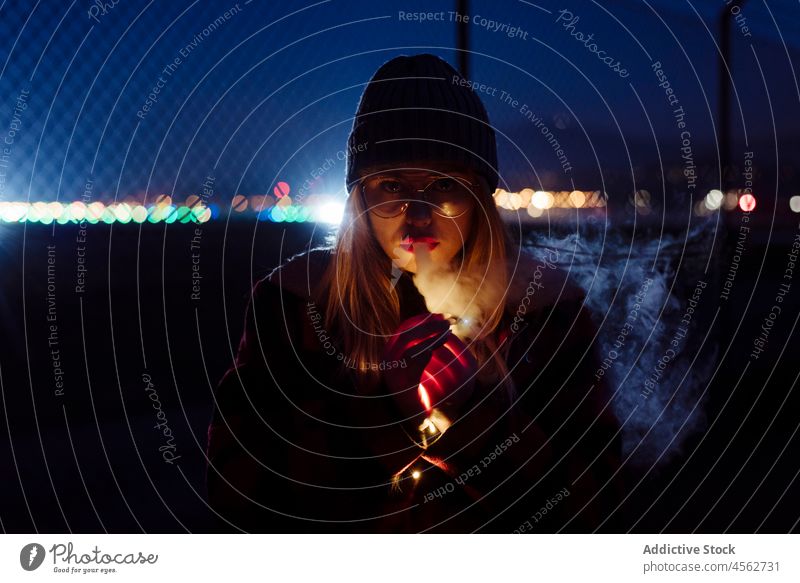 Junge Frau mit Wollmütze und Brille hält eine leichte Girlande jung Nacht Porträt attraktiv Herbst blond Bokeh Glühbirnen offen Kaukasier Großstadt kalt