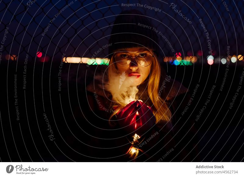 Junge Frau mit Wollmütze und Brille hält eine leichte Girlande jung Porträt Nacht attraktiv Herbst blond Bokeh Glühbirnen offen Kaukasier Großstadt kalt