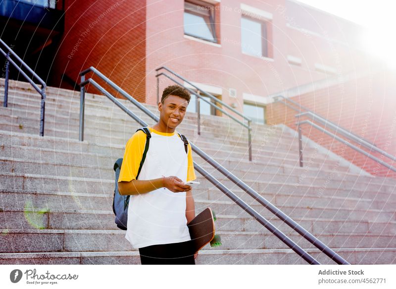 Junge schwarze Studentin benutzt Smartphone auf der Straße jung männlich Mann Glück laufen ethnisch Lächeln Skateboard benutzend Afrikanisch