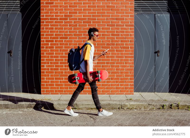 Junger schwarzer Mann geht mit Kopfhörern und hört Musik auf der Straße jung männlich benutzend Telefon Smartphone Spaziergang Browsen Gerät Handy