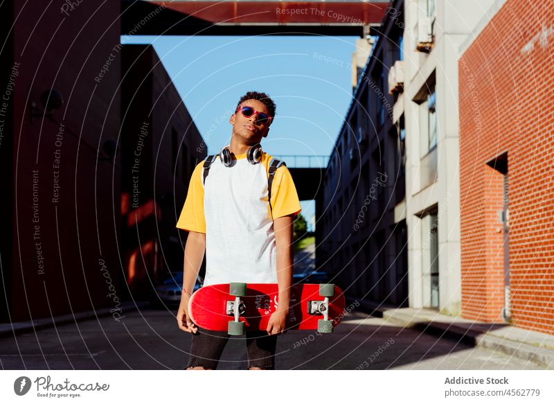 Junger schwarzer Mann mit Skateboard auf der Straße Schüler Schule Teenager Tageslicht horizontal Großstadt Freizeit Lifestyle männlich Sonnenbrille attraktiv
