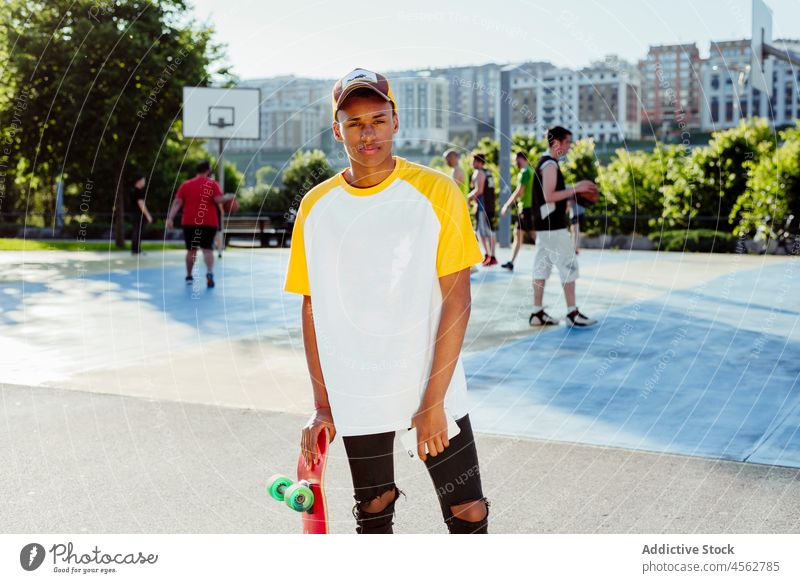 Junger schwarzer Mann mit T-Shirt und Mütze posiert im Park jung männlich konzentriert Verschlussdeckel Straße Porträt urban Großstadt Skateboard gutaussehend