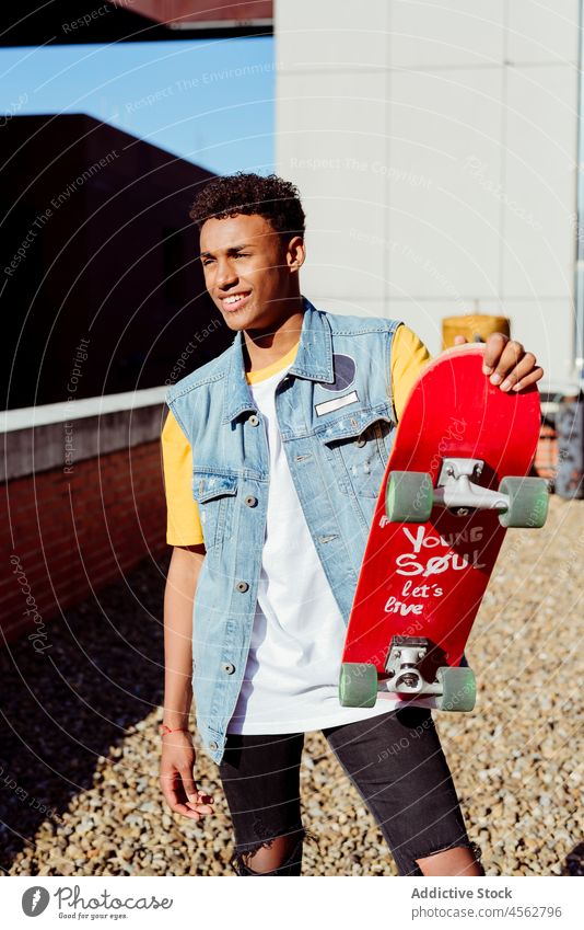 Hübscher junger schwarzer Mann mit einem Skateboard auf der Straße männlich Junge Glück Lächeln Porträt Backstreet urban Großstadt Baustein Wand Dachterrasse