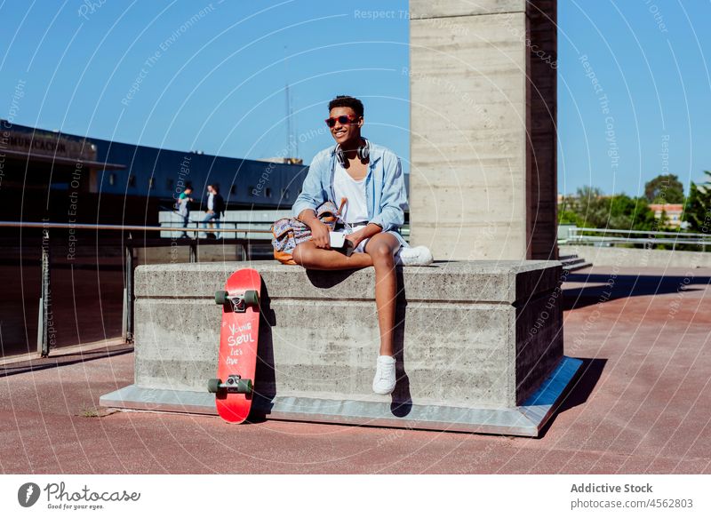 Junger schwarzer Mann sitzt auf einer Bank und telefoniert männlich jung gemischt sitzen Teenager benutzend Telefon Skateboard Schule im Freien Afrikanisch