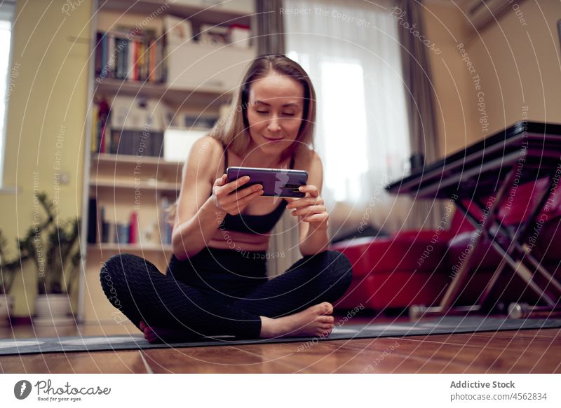 Frau in Sportkleidung sieht sich beim Yoga-Training ein Video an Gesunder Lebensstil Übung Wellness Smartphone Browsen online Funktelefon Wohlbefinden üben