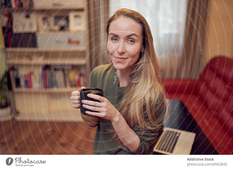 Fröhliche Frau mit Kaffee im Zimmer Heißgetränk Wohnzimmer heimisch Appartement Liege Laptop Getränk heimwärts Sofa positiv Netbook Dame Licht Tasse Inhalt