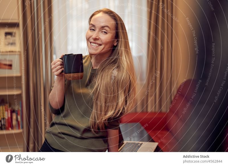 Lächelnde Frau mit Kaffee im Zimmer Heißgetränk Wohnzimmer heimisch Appartement Liege Laptop Getränk heimwärts Sofa positiv Netbook Dame Licht Tasse Inhalt