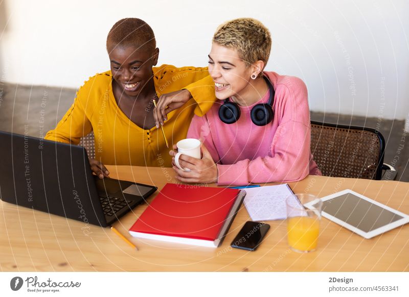 Multiethnische lächelnde Frauen, die im Büro zu Hause einen Laptop benutzen Paar Person Computer Sitzen Lächeln heimwärts im Innenbereich Zusammensein Lifestyle