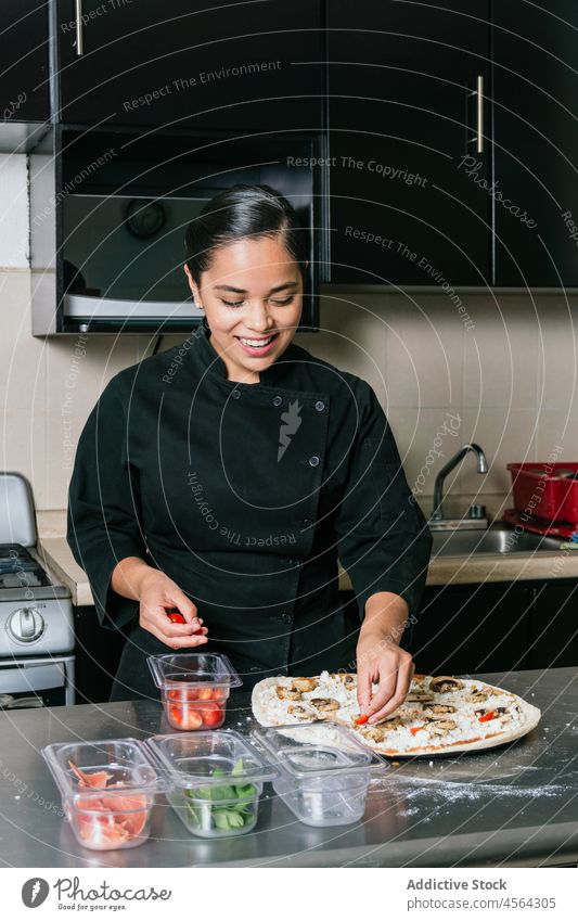 Lächelnde ethnische Köchin beim Pizzabacken Frau Tomate Küchenchef Koch professionell hinzufügen Restaurant Lebensmittel vorbereiten Job kulinarisch Beruf